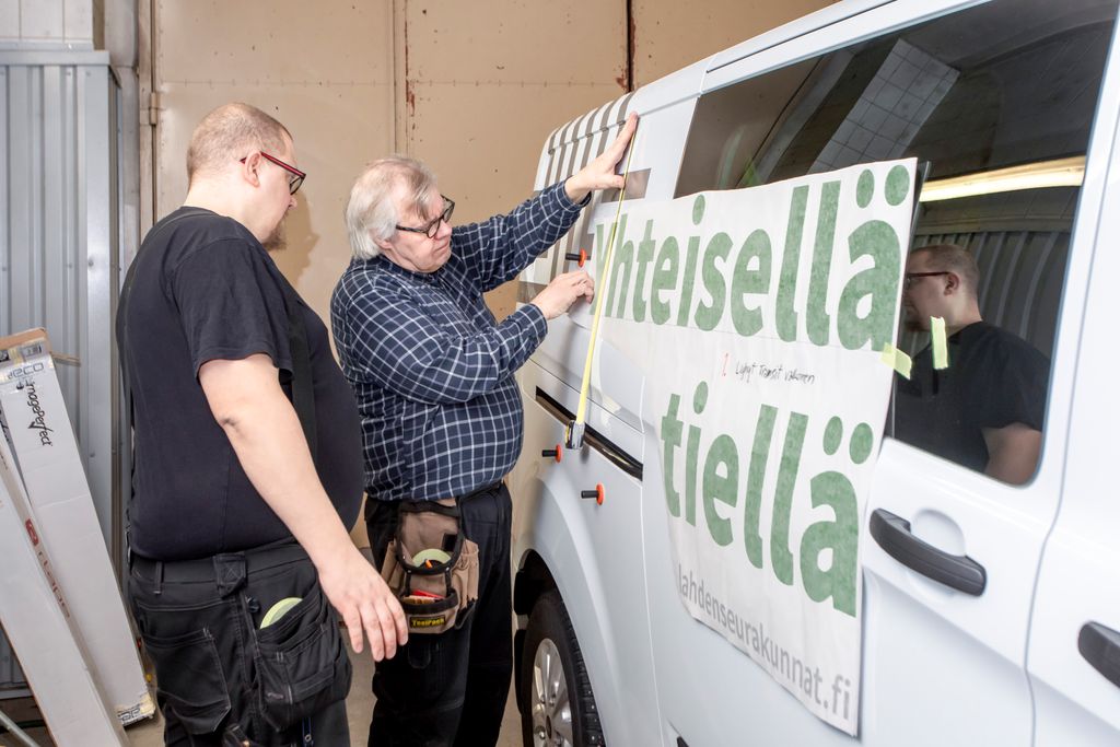 Lahden seurakuntien uusi ilme näkyy esimerkiksi katukuvassa kaikille lahtelaisille. Mainosteippausyrityksen Joonas Arvelinin ja Heikki Arvelin asensivat uutta tunnuslausetta seurakunnan pakettiautoon. Kuva: Markku Lehtinen